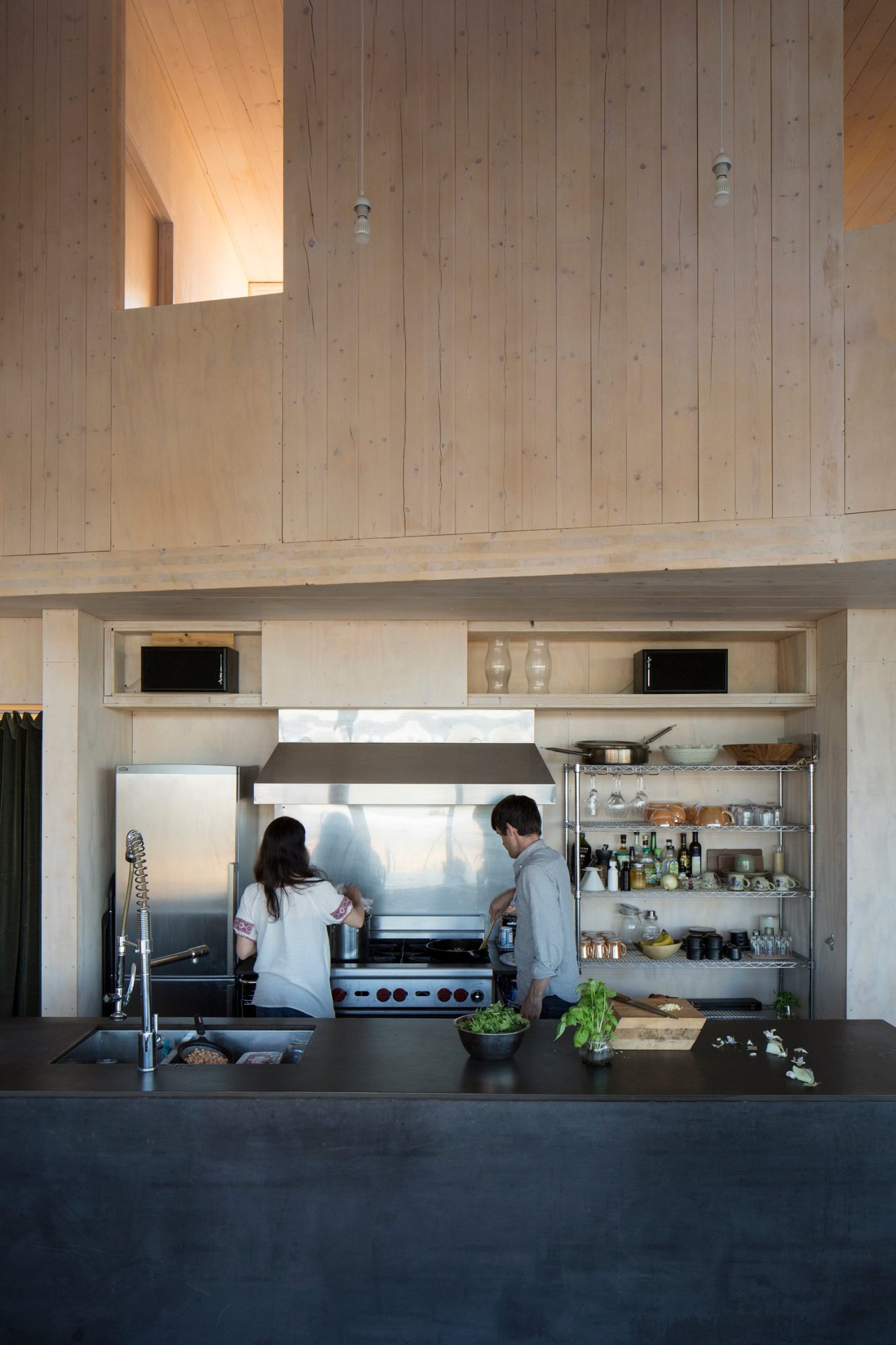 Kitchen with steel counters and open shelving under a tall timber wall
