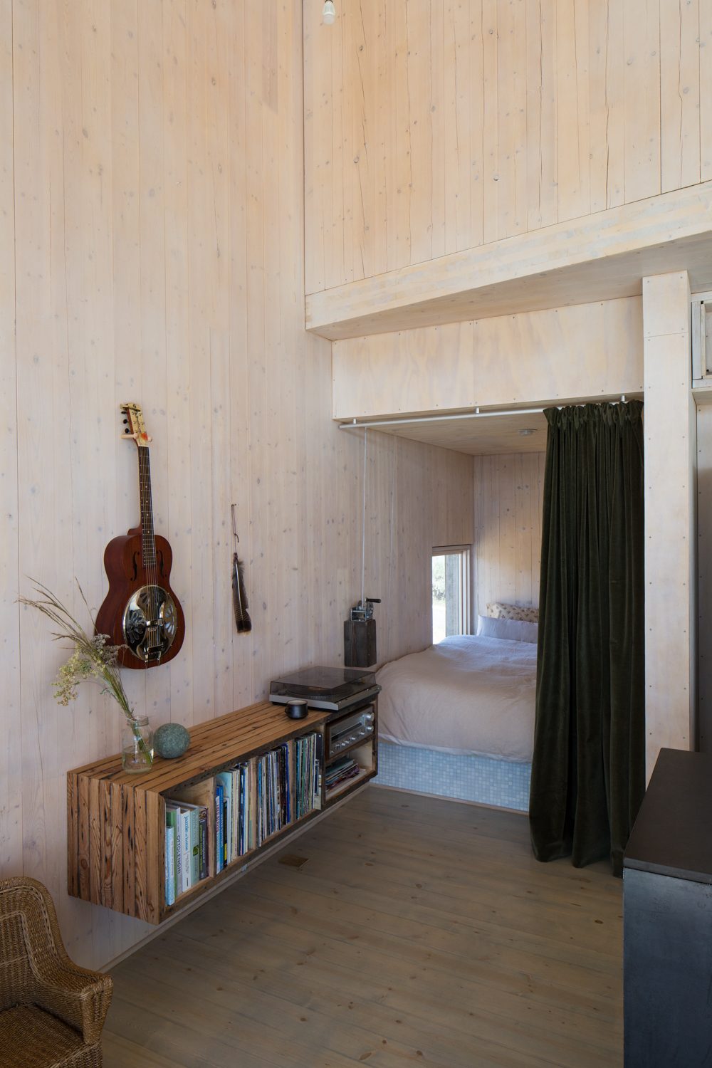 Sleeping alcove behind a green velvet curtain beside a record shelf